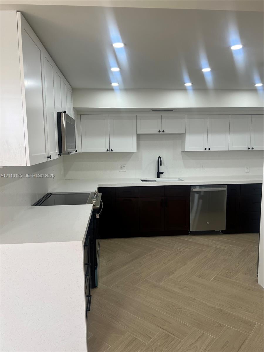 Kitchen featuring white upper cabinetry, dark base cabinetry, solid surface countertops, a matte black faucet, and wood-finish herringbone flooring