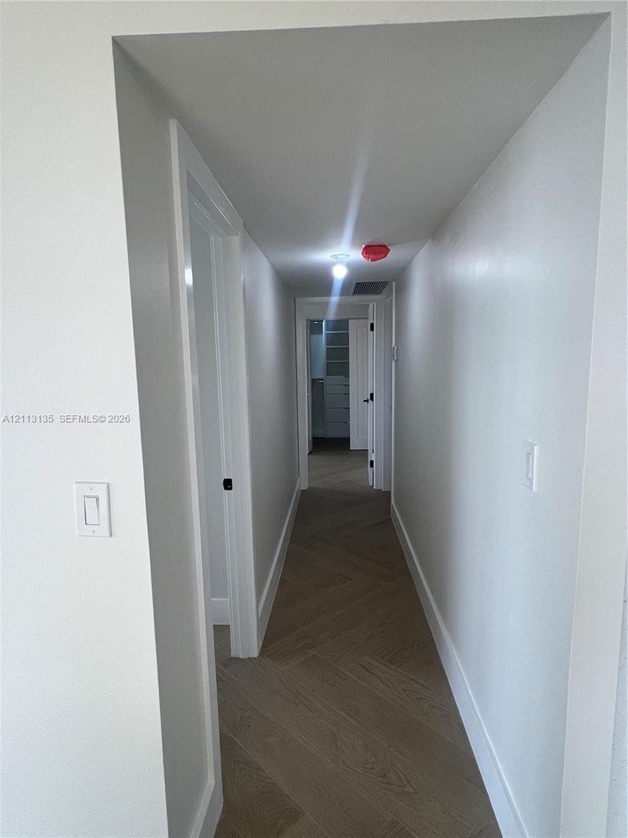 Hallway featuring herringbone-pattern wood-finish flooring, white walls, and interior passage doors
