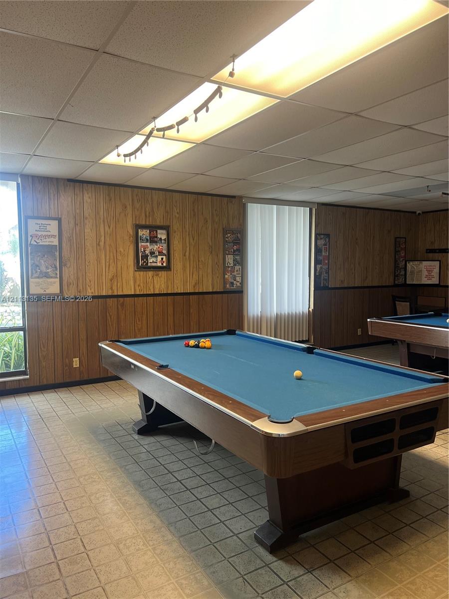 Wood-panelled wall treatments with chair rail molding, drop ceiling with integrated fluorescent lighting, and tile flooring