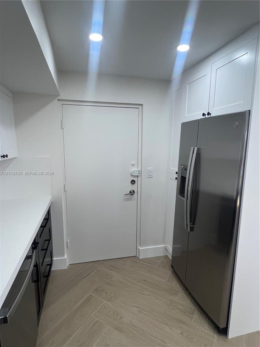 Shaker-style white cabinetry, stainless steel side-by-side refrigerator, solid-surface countertops, recessed lighting, and herringbone-patterned flooring