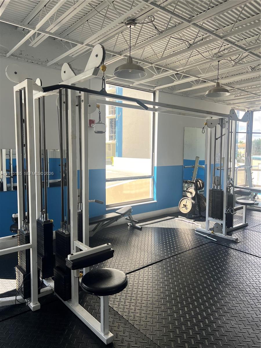Fitness facility featuring high, exposed-joist ceilings, industrial-style pendant lighting, rubberized diamond-plate flooring, and large windows