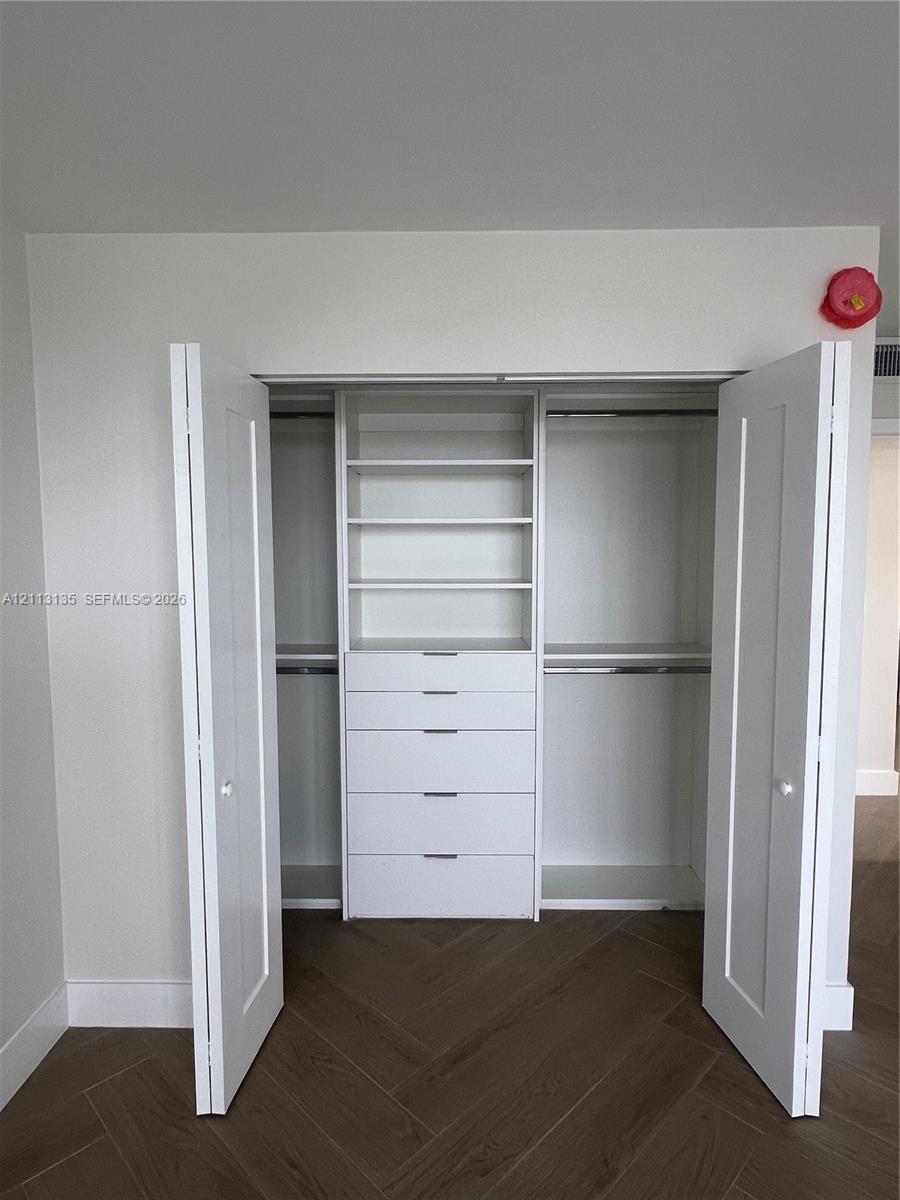 Closet featuring white dual-panel doors, built-in shelving, integrated dresser drawers, and metal hanging rods over wood-finish flooring