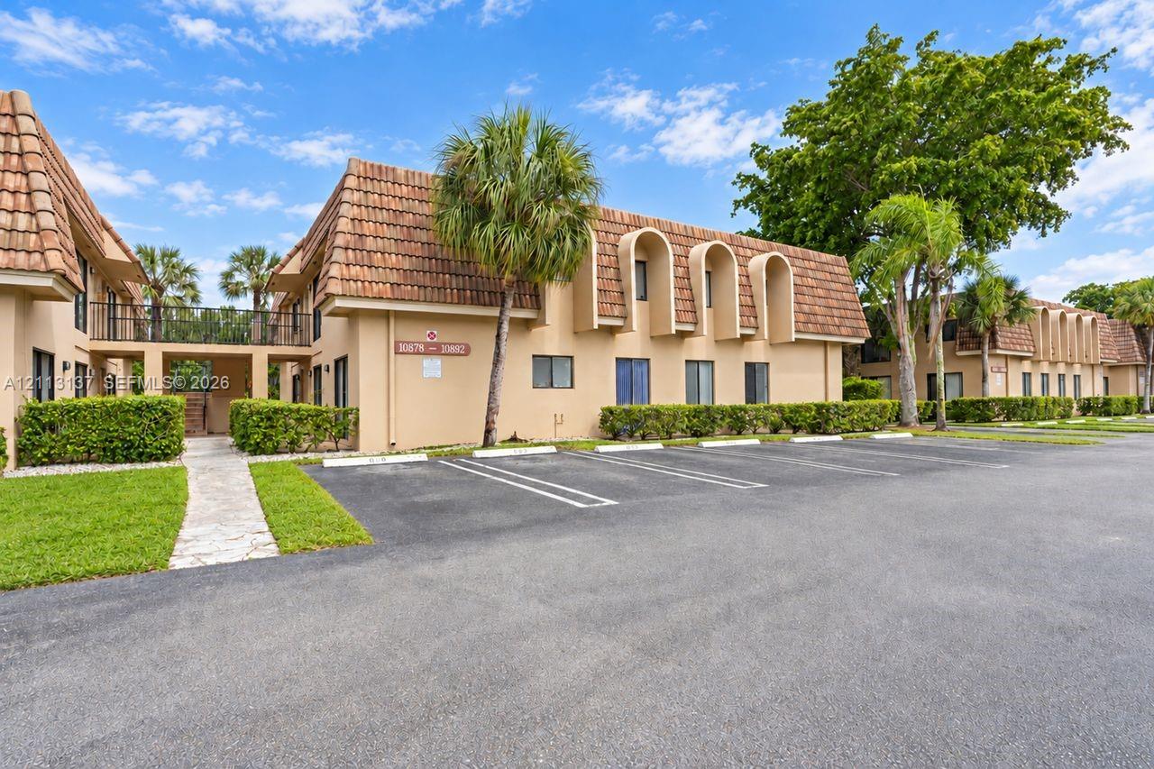 Two-story exterior featuring a clay tile roof, arched architectural accents, beige stucco finish, designated surface parking, and manicured perimeter landscaping Two-story exterior featuring a clay tile roof, arched architectural accents, beige stucco finish, designated surface parking, and manicured perimeter landscaping