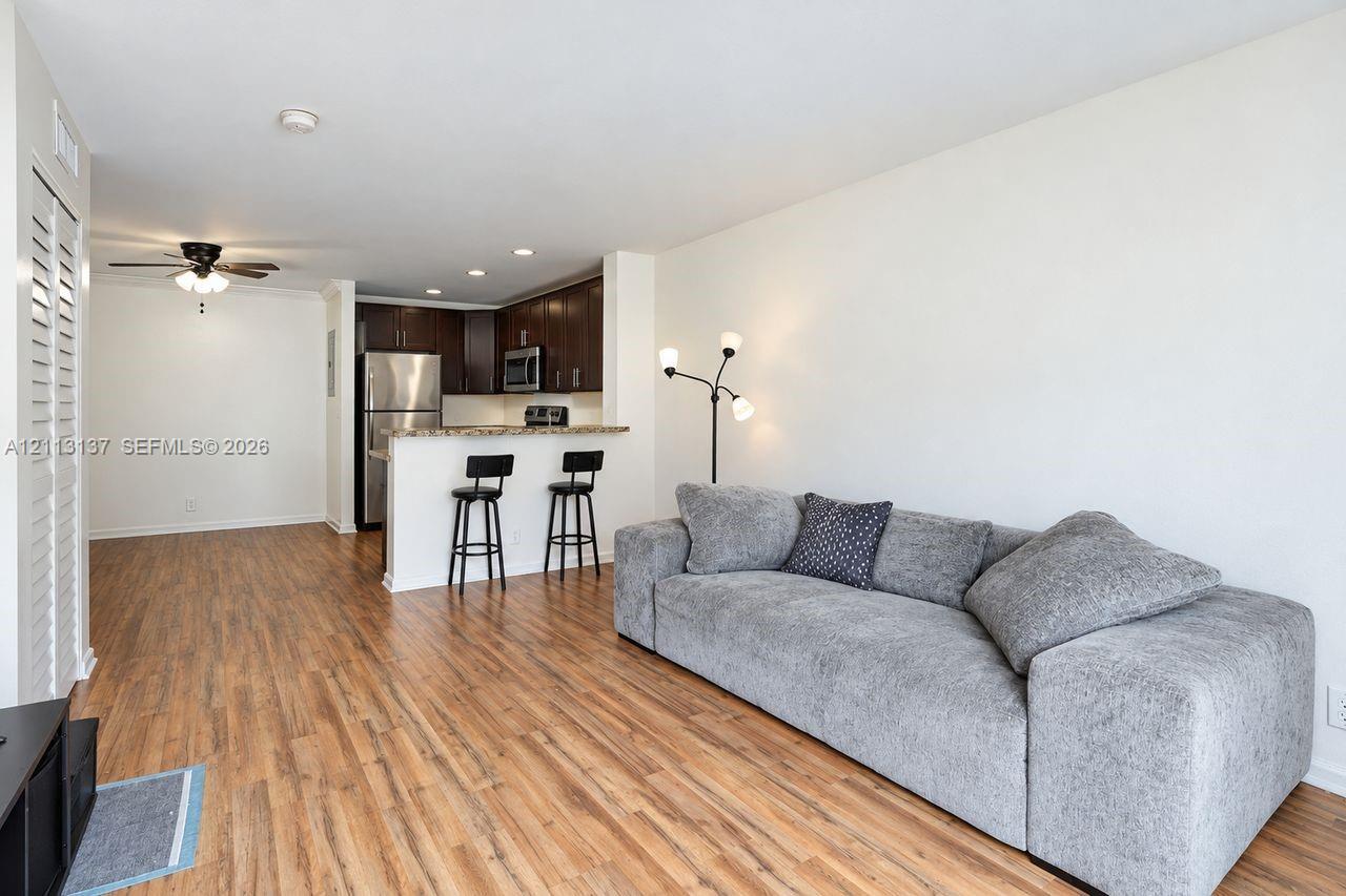 Open-concept interior featuring wood-finish flooring, dark wood cabinetry, stainless steel kitchen appliances, stone-surface breakfast bar, and recessed lighting