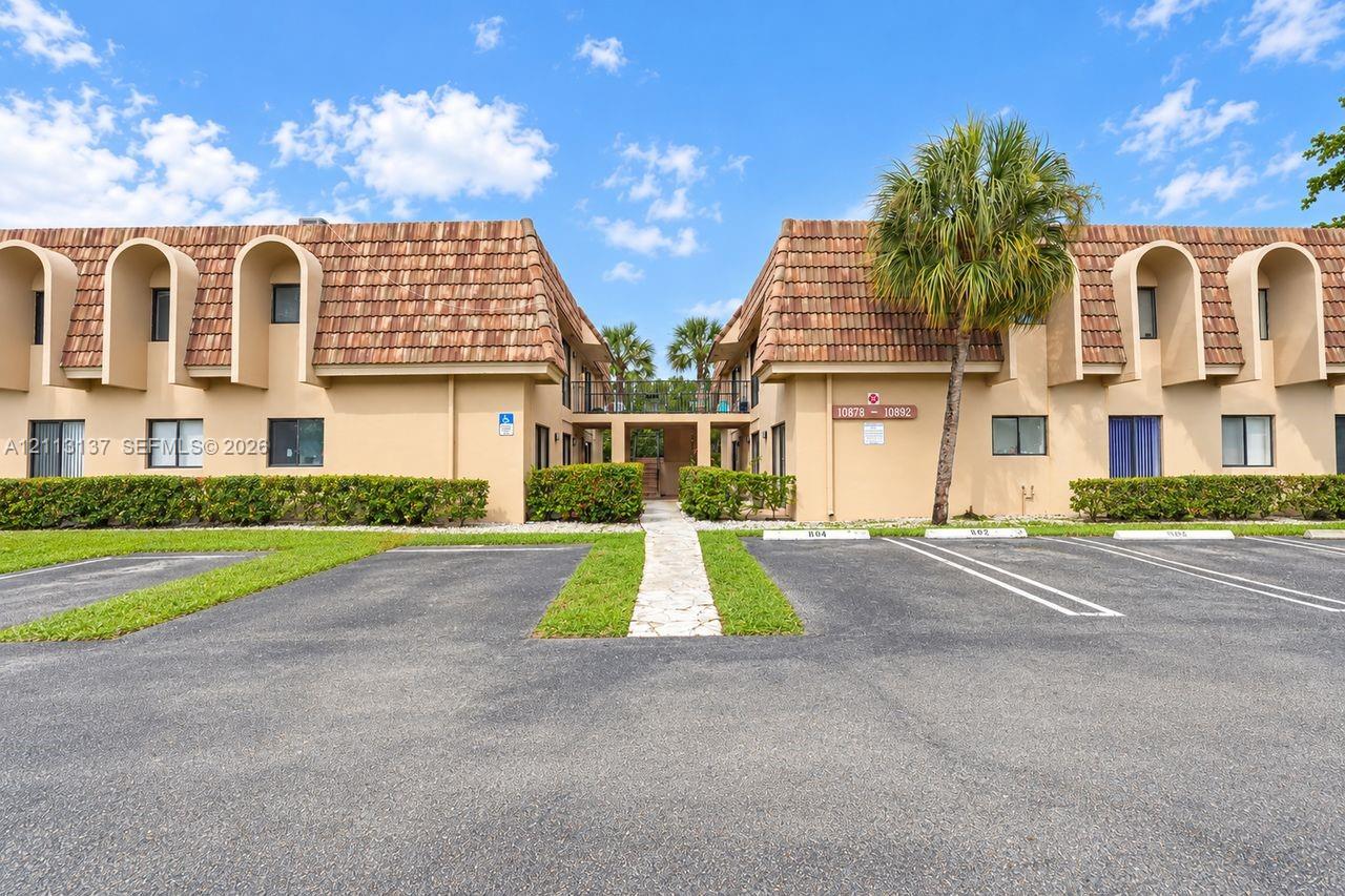 Exterior featuring a mansard roof, arched window surrounds, stucco facade, paved parking lot, and manicured landscaping Exterior featuring a mansard roof, arched window surrounds, stucco facade, paved parking lot, and manicured landscaping