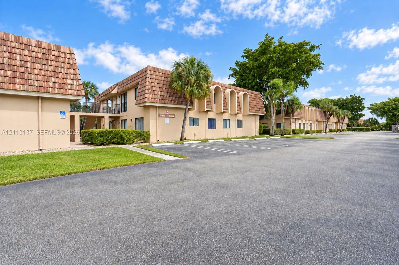 Two-story exterior featuring a clay tile roof, arched architectural details, stucco siding, paved parking area, and landscaped grounds Two-story exterior featuring a clay tile roof, arched architectural details, stucco siding, paved parking area, and landscaped grounds