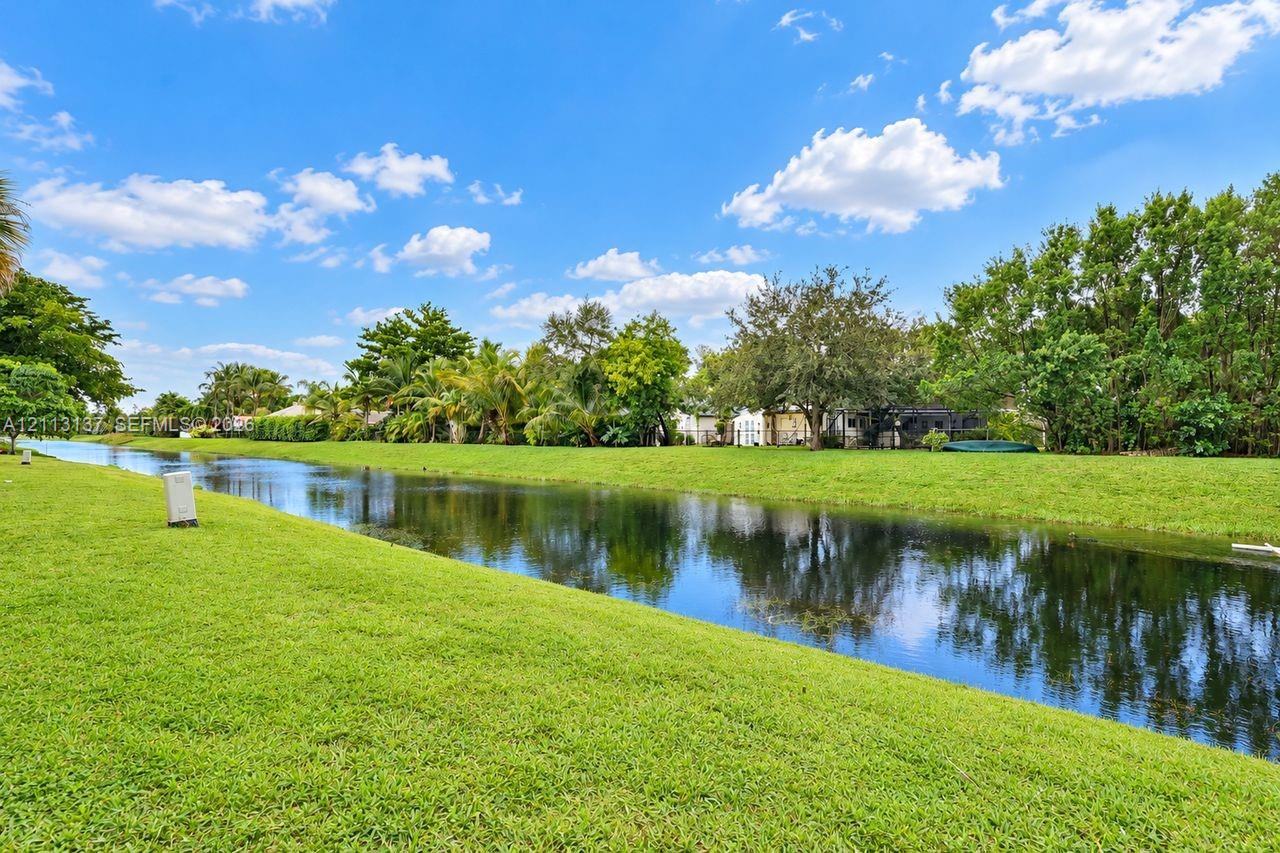 Waterfront lot featuring a grass lawn, canal frontage, and mature landscaping Waterfront lot featuring a grass lawn, canal frontage, and mature landscaping