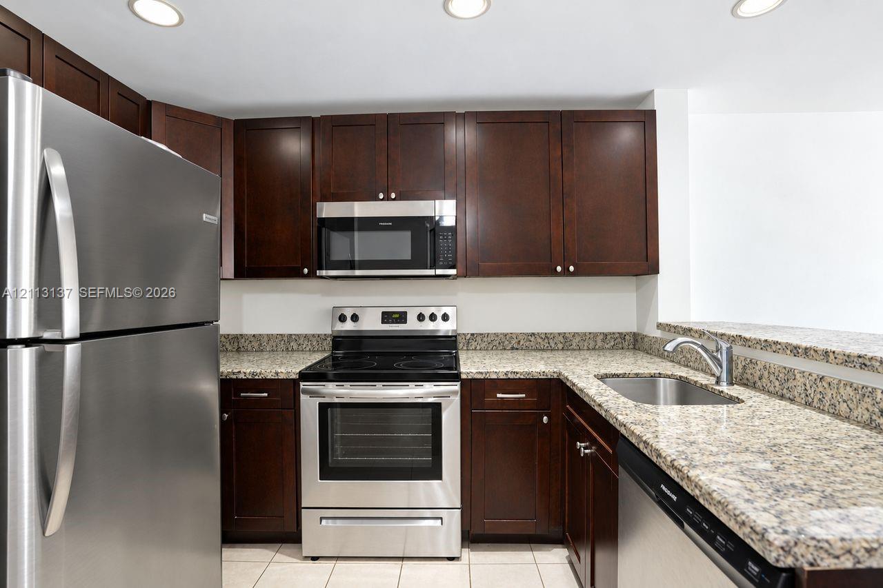 Kitchen featuring dark wood-finish cabinetry, speckled stone countertops, stainless steel appliances, recessed ceiling lighting, and tile flooring