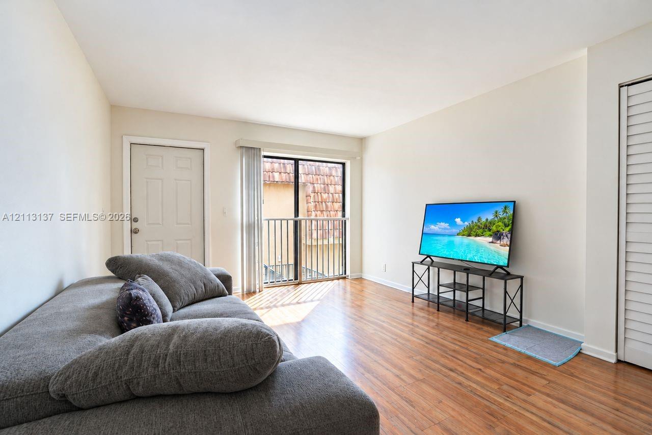 Living area featuring wood-finish flooring, neutral wall paint, and a sliding glass door providing access to a metal-railed balcony