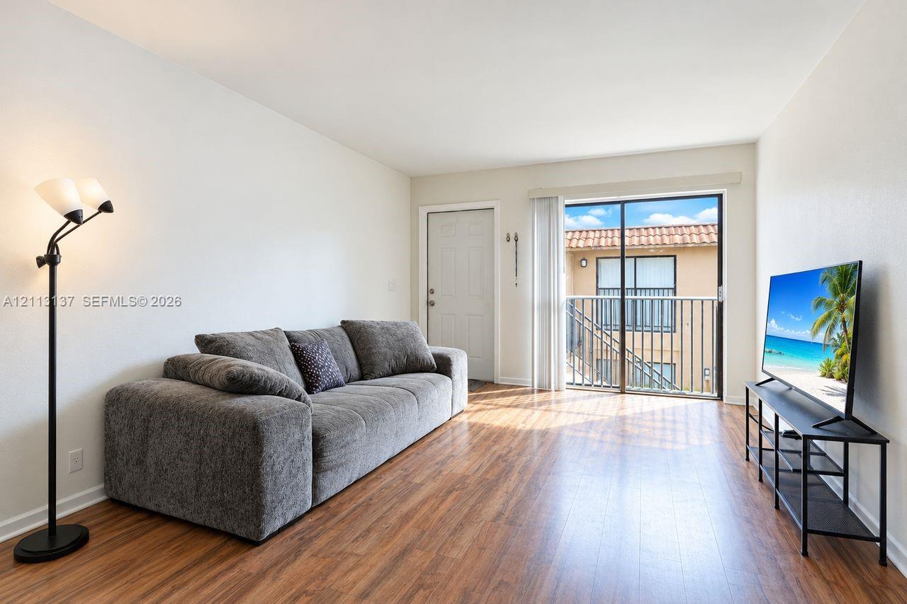 Living area featuring wood-finish flooring, neutral wall paint, and a sliding glass door providing access to a private balcony with a metal railing