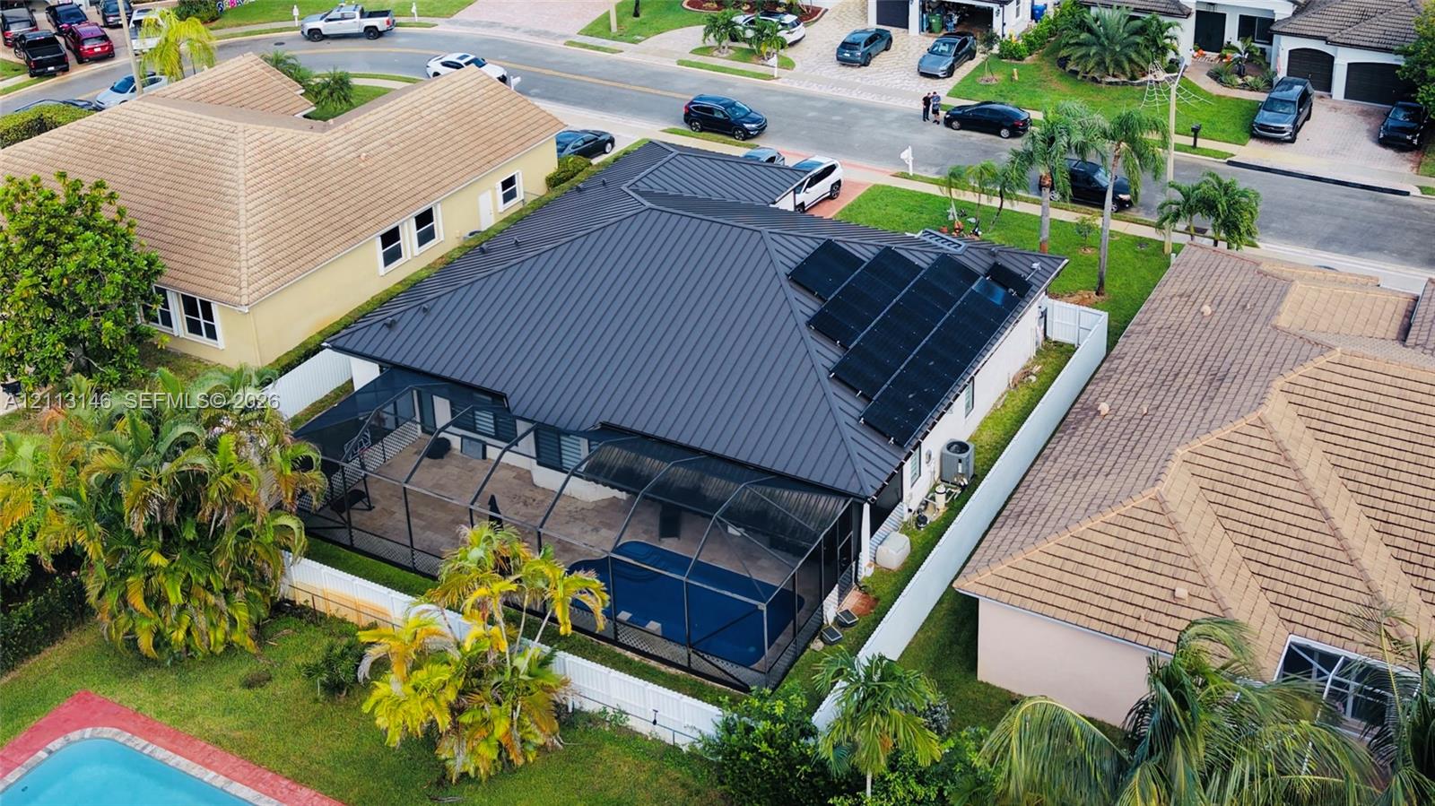 Metal roof featuring integrated solar panels, a screened-in swimming pool enclosure, and fenced perimeter Metal roof featuring integrated solar panels, a screened-in swimming pool enclosure, and fenced perimeter