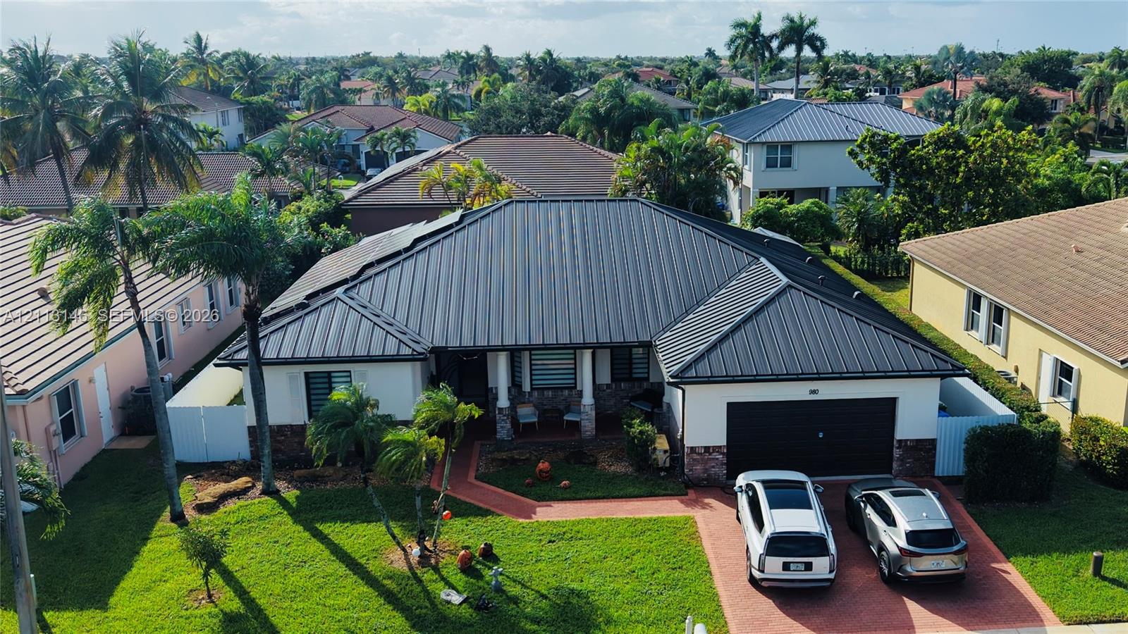 Single-story residence featuring a standing-seam metal roof, stucco exterior with stone veneer accents, an attached two-car garage, and a paved driveway