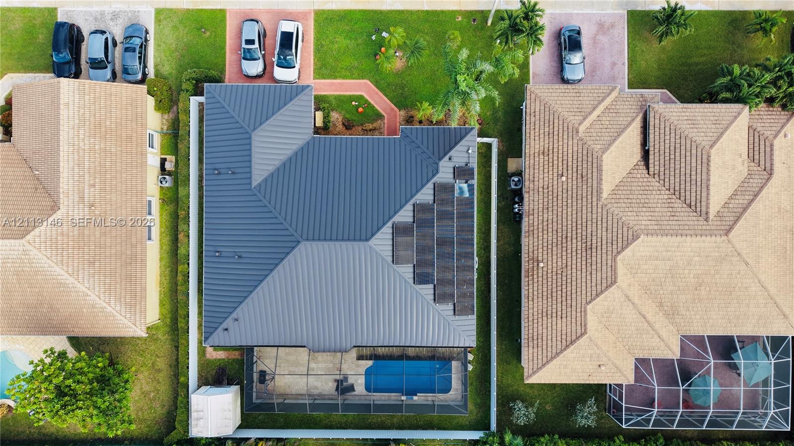 Aerial perspective featuring a metal roof, integrated solar panels, a screened-in swimming pool, and a paved walkway Aerial perspective featuring a metal roof, integrated solar panels, a screened-in swimming pool, and a paved walkway