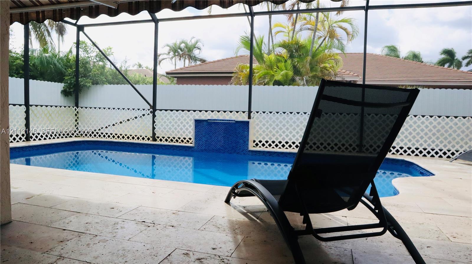 Screened-in pool area featuring a stone-paver deck, blue tile water feature, and lattice privacy fencing Screened-in pool area featuring a stone-paver deck, blue tile water feature, and lattice privacy fencing