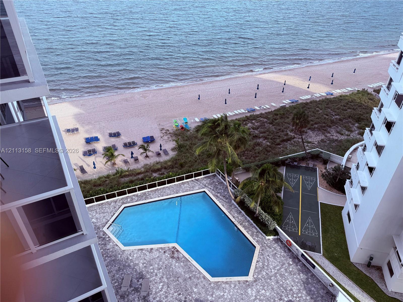 Elevated perspective featuring an outdoor swimming pool, paved pool deck, shuffleboard court, and direct shoreline access