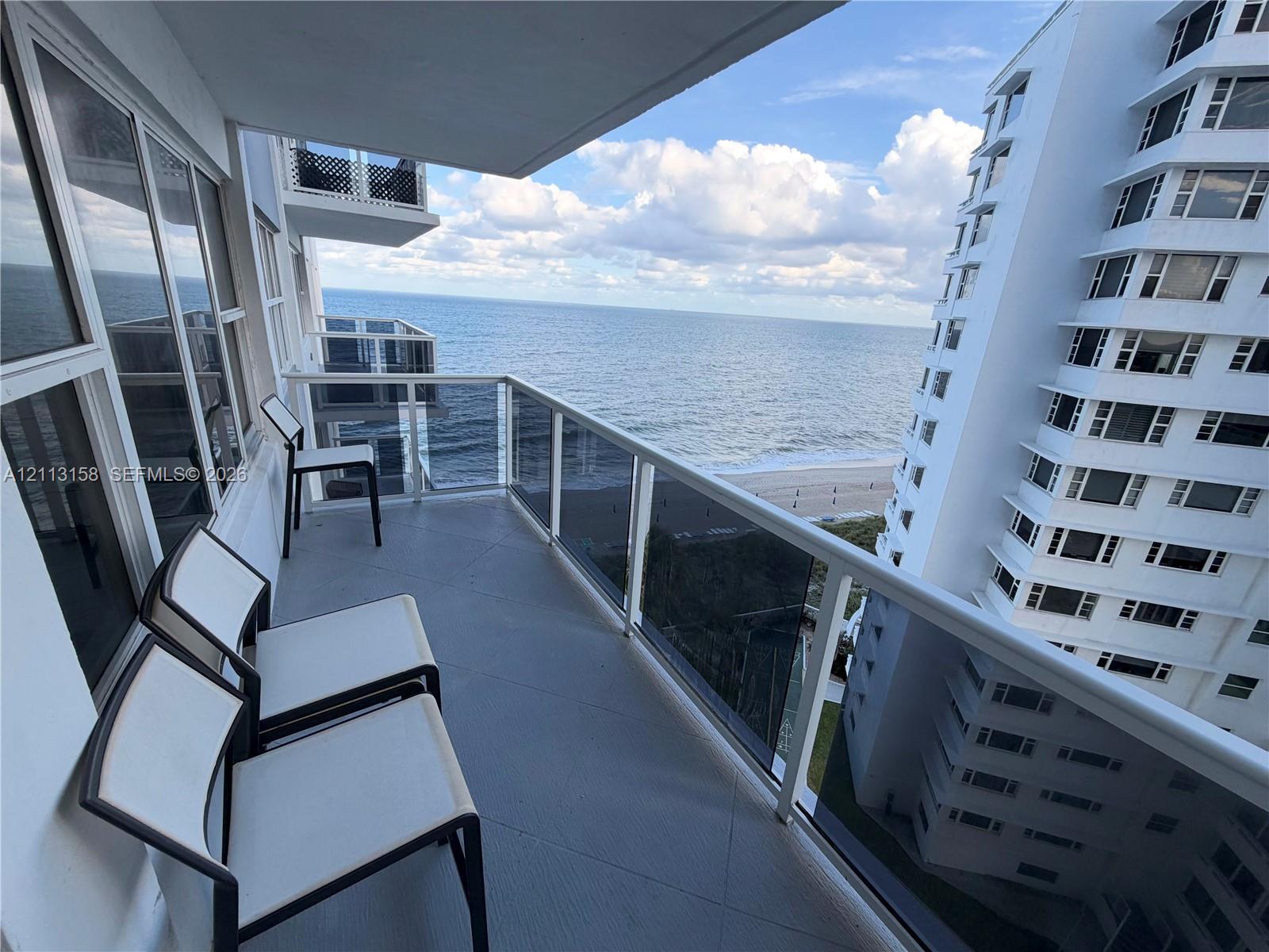 Private balcony featuring a glass-panel railing, floor-to-ceiling windows, and oceanfront exposure