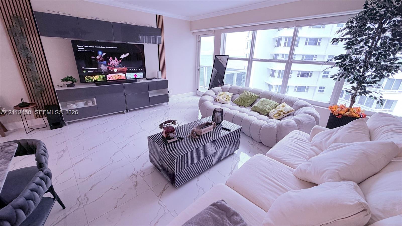 Living area featuring polished tile flooring, floor-to-ceiling windows, and custom wall-mounted cabinetry with integrated vertical wood slat paneling