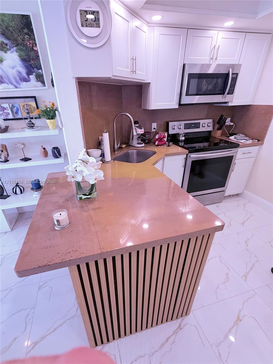 Kitchen featuring a slatted wood-finish island base, solid-surface countertop, white shaker-style cabinetry, stainless steel appliances, and tile flooring Kitchen featuring a slatted wood-finish island base, solid-surface countertop, white shaker-style cabinetry, stainless steel appliances, and tile flooring