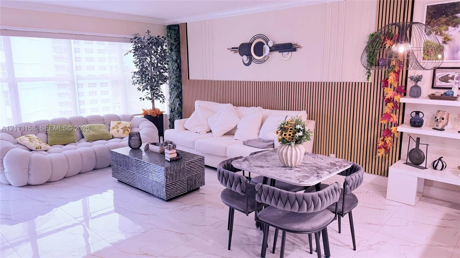 Living area featuring large-format tile flooring, vertical wood-slat accent wall detailing, floor-to-ceiling windows, and white built-in shelving