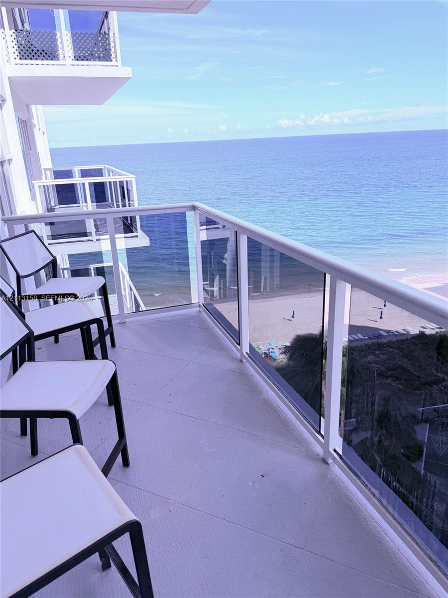 Covered balcony featuring white railings, tempered glass panels, and solid flooring with an ocean backdrop Covered balcony featuring white railings, tempered glass panels, and solid flooring with an ocean backdrop