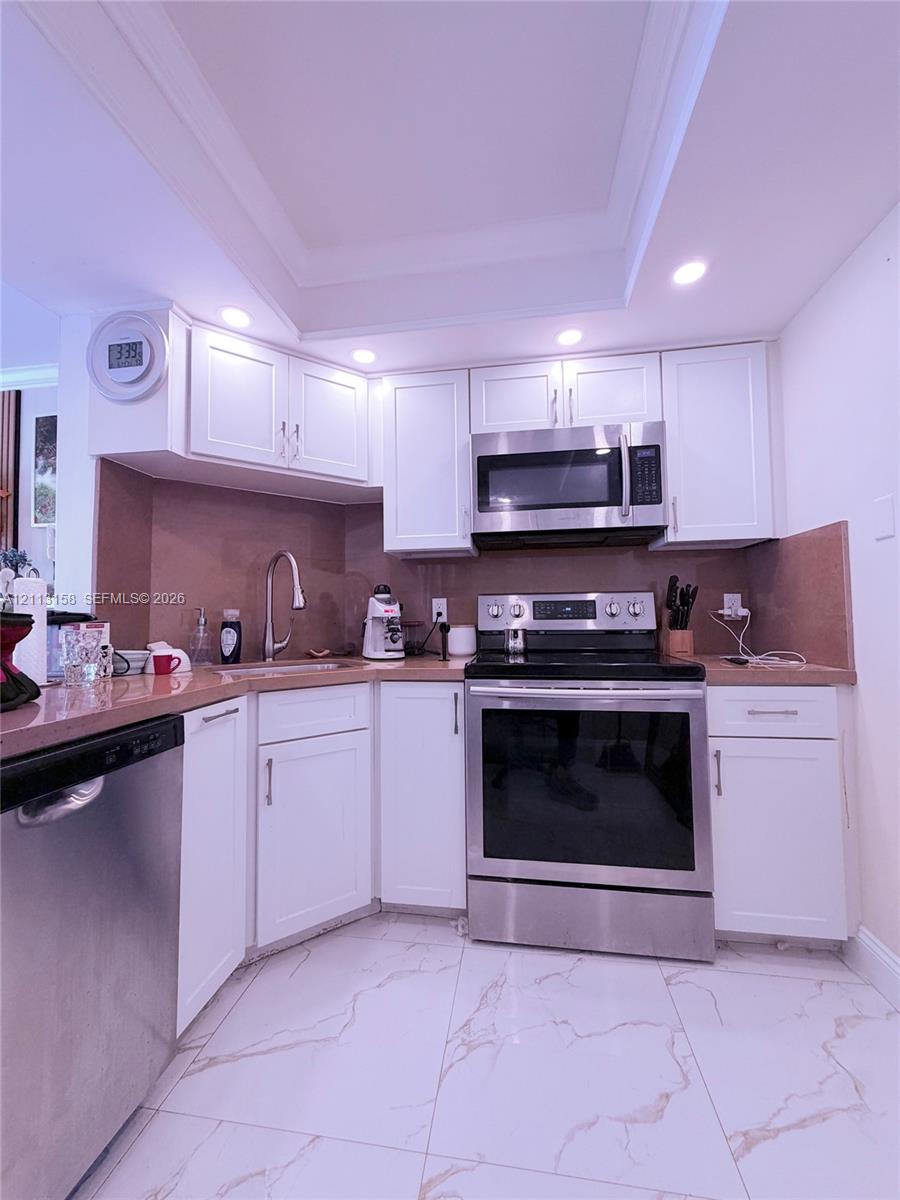 Kitchen featuring white shaker-style cabinetry, stainless steel appliances, solid surface countertops, a high-arch gooseneck faucet, and large-format flooring with a veined pattern