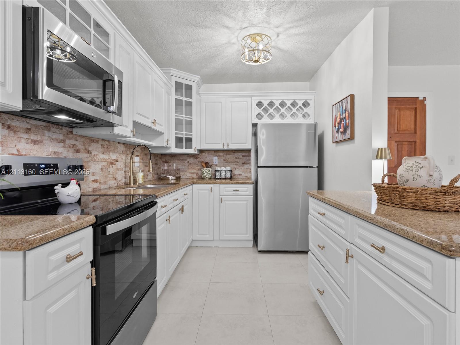 Kitchen featuring white shaker-style cabinetry, stone-finish countertops, stainless steel appliances, brick-style tile backsplash, and a built-in wine rack