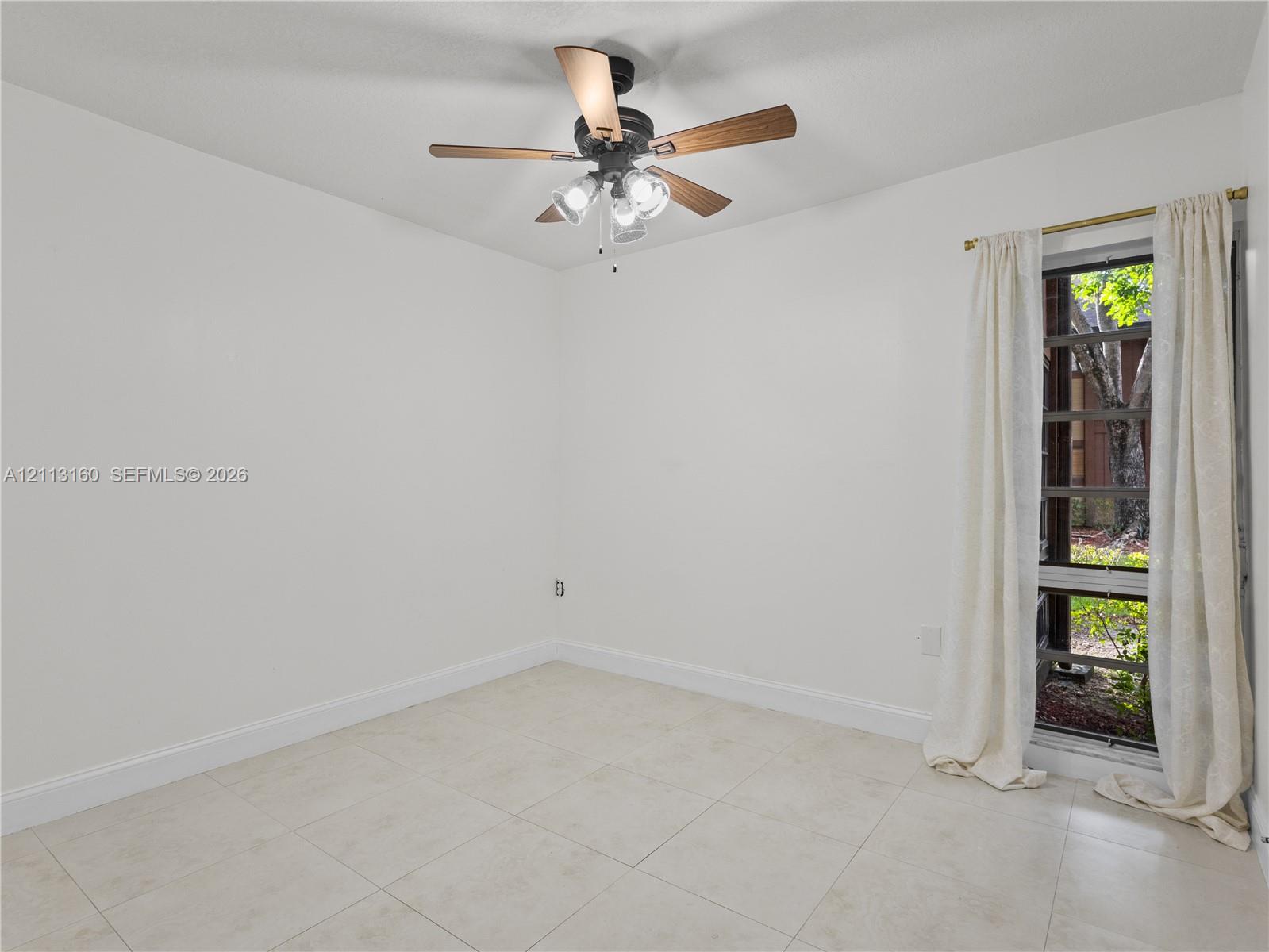 Neutral tile flooring, multi-light ceiling fan with wood-finish blades, and tall window with black-frame muntins