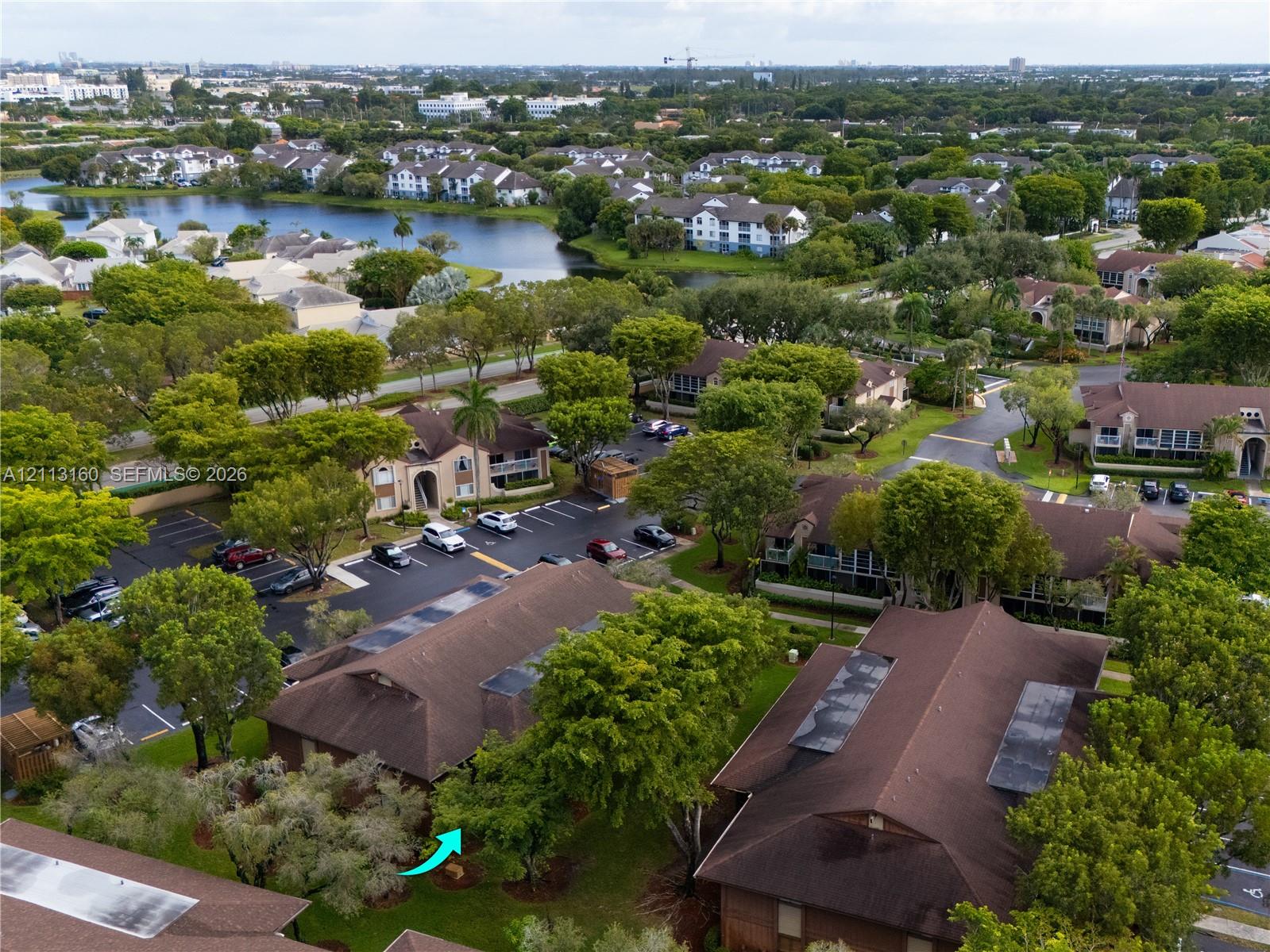 Aerial perspective of multi-family structures featuring brown shingle roofing, integrated skylights, and mature tree-lined landscaping within a planned community setting