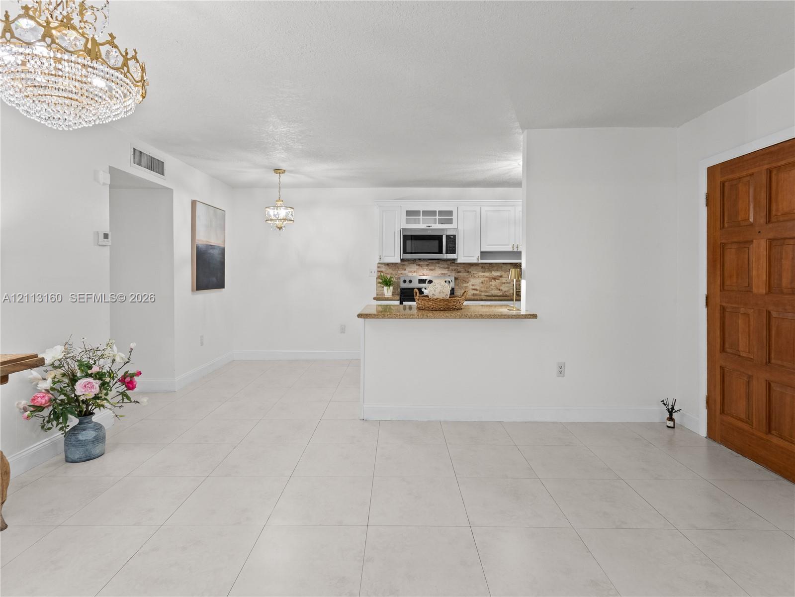 Kitchen featuring white shaker-style cabinetry, stone-surface countertops, built-in microwave, and tile flooring throughout, accented by decorative chandeliers