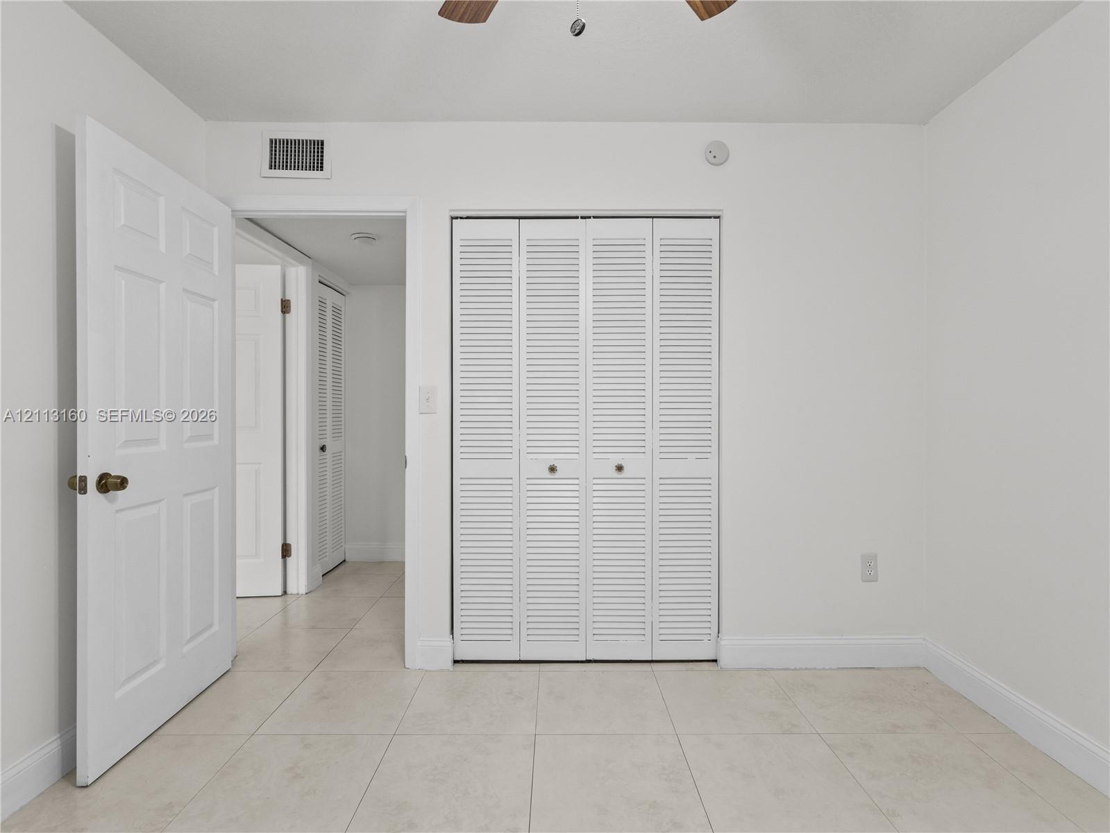 Neutral tile flooring, white six-panel interior doors, and closet featuring white bi-fold louvered doors