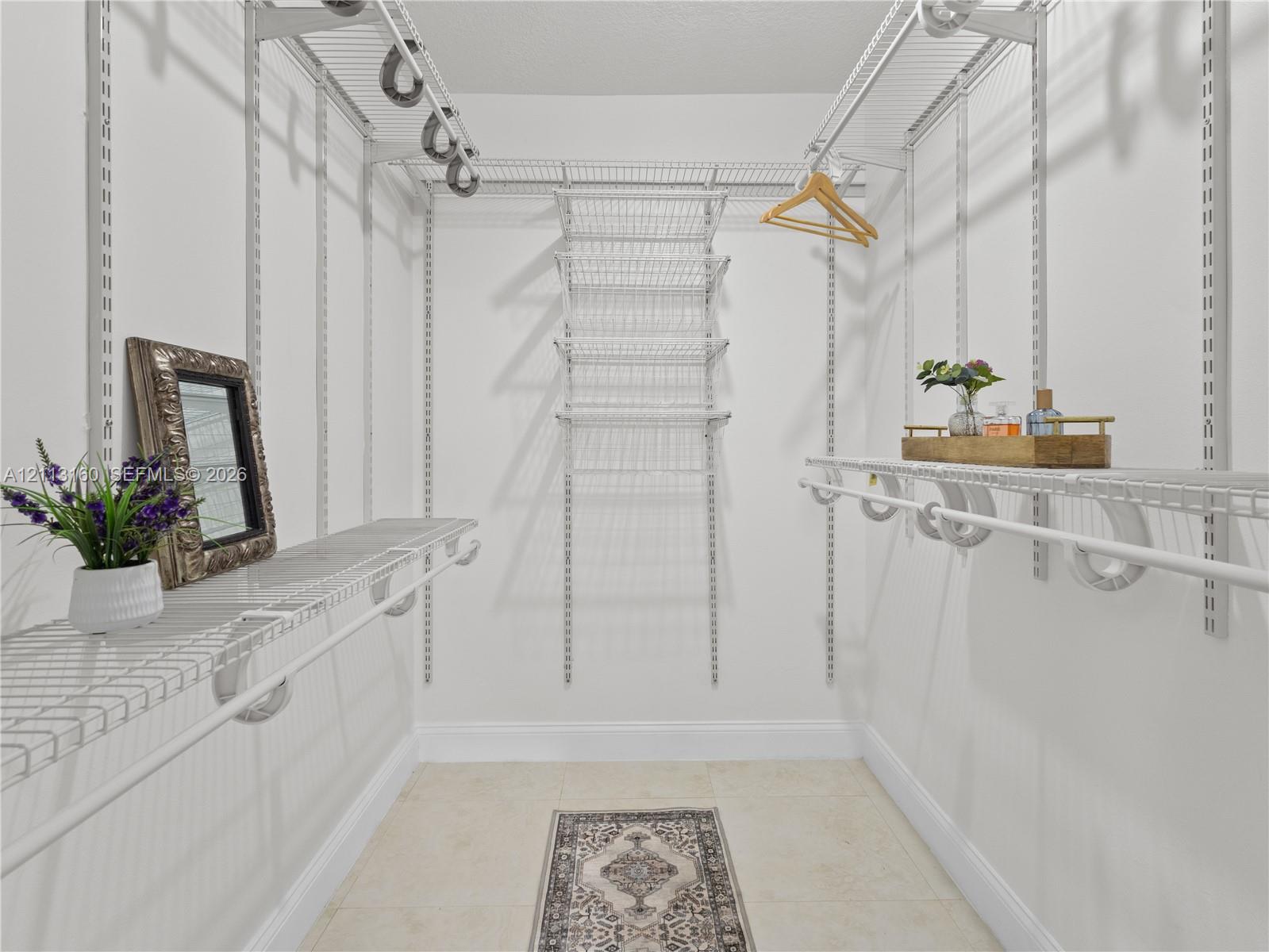 Walk-in closet featuring adjustable white wire shelving, wall-mounted vertical track supports, and neutral tile flooring
