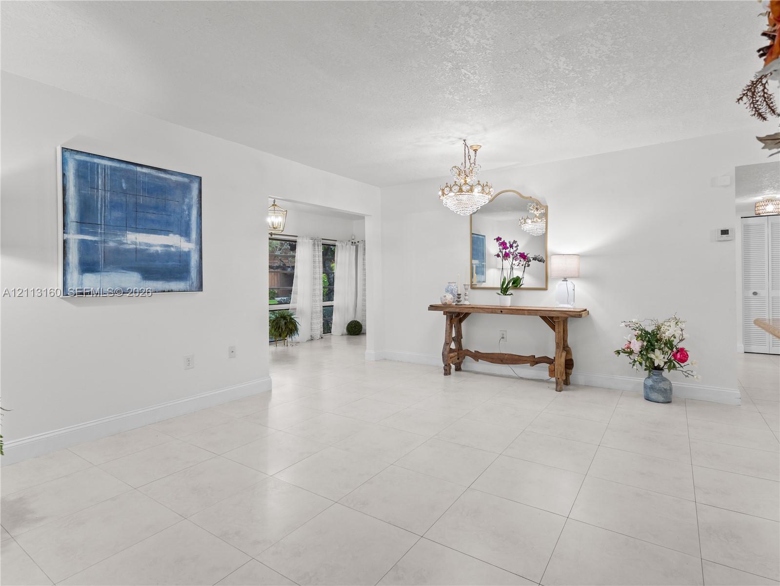 Neutral ceramic tile flooring, crystal chandelier, and large-format wall opening