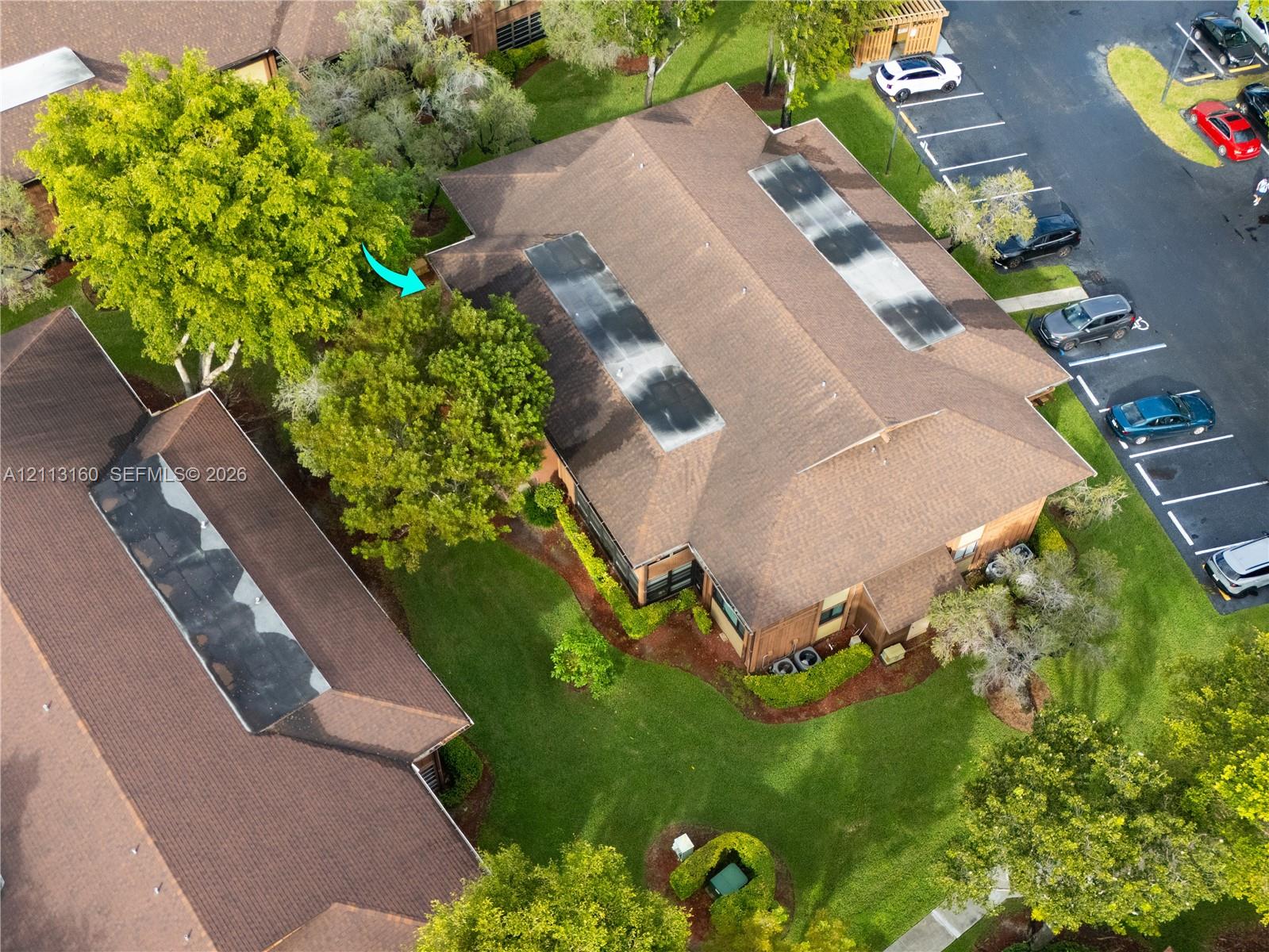 Aerial perspective featuring a multi-hipped shingled roof, skylight fixtures, masonry siding, and landscaped grounds with mature trees