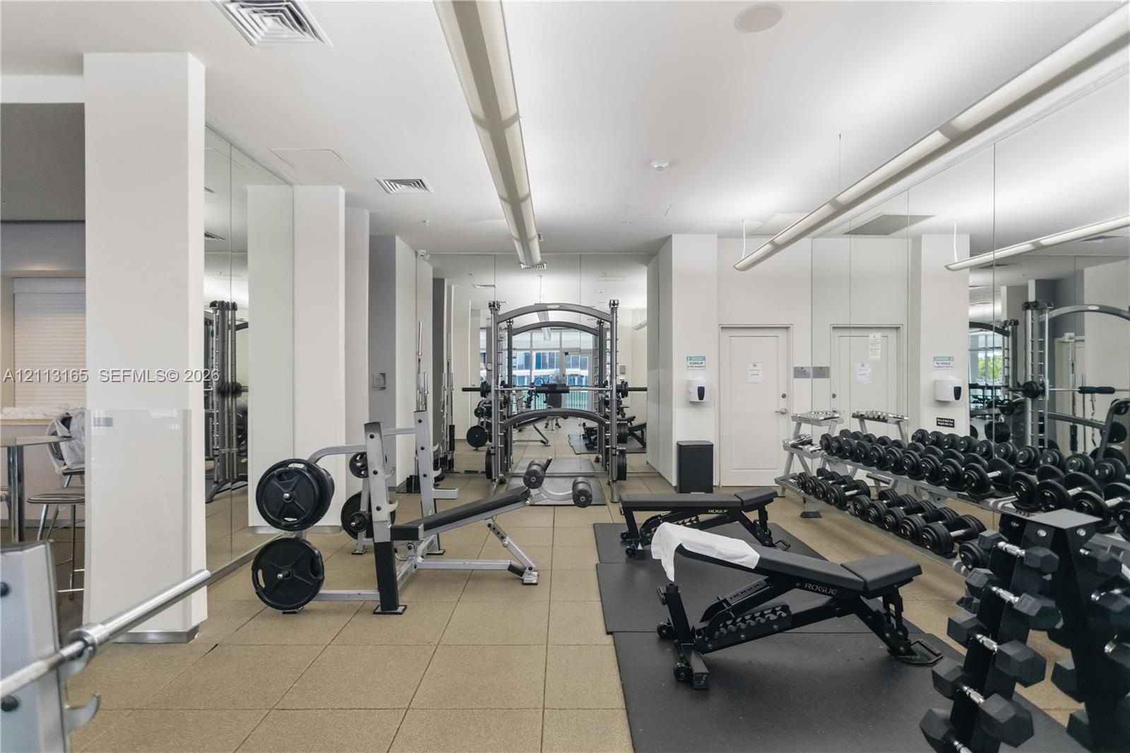 Fitness facility featuring industrial-style suspended lighting, full-length wall mirrors, and textured tile flooring