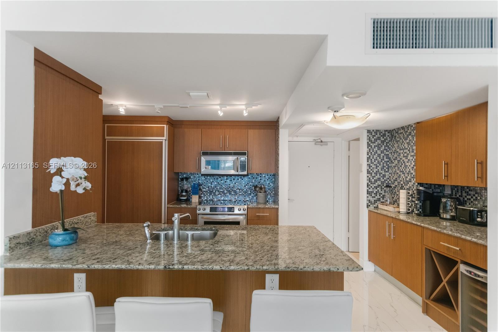 Kitchen featuring wood-finish cabinetry, stone countertops, mosaic tile backsplash, built-in stainless steel appliances, and a dedicated wine storage rack