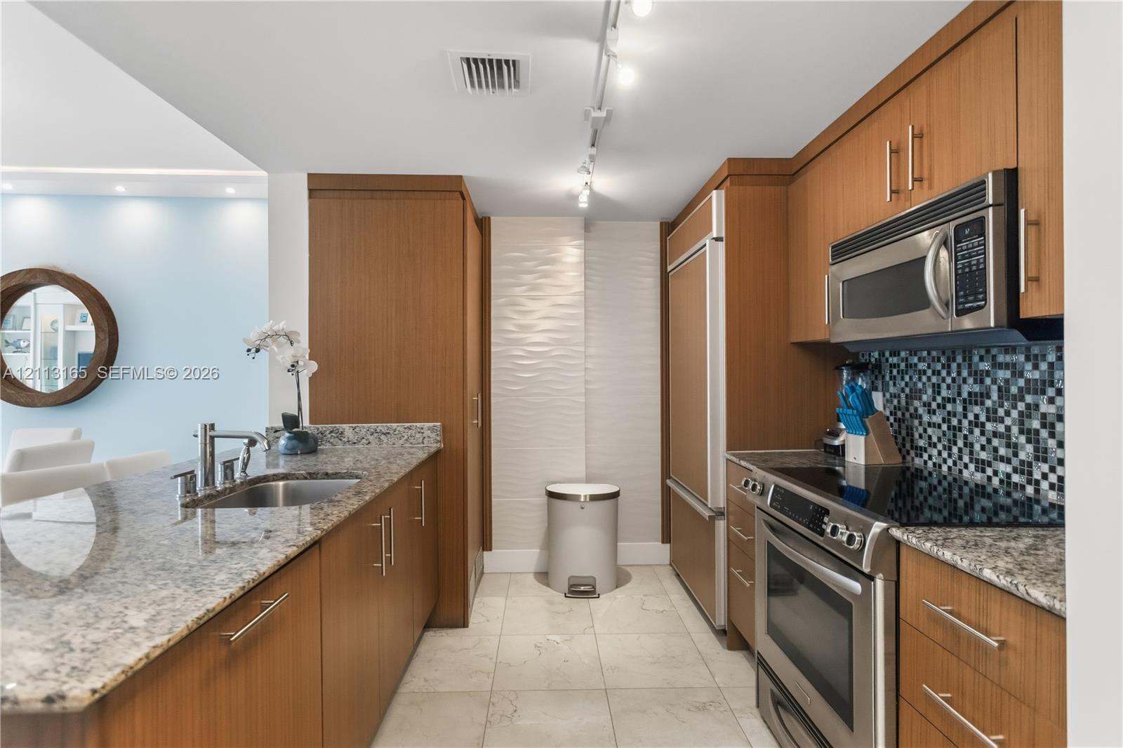 Kitchen featuring wood-finish cabinetry, stone countertops, stainless steel appliances, a tile backsplash, and stone-finish flooring