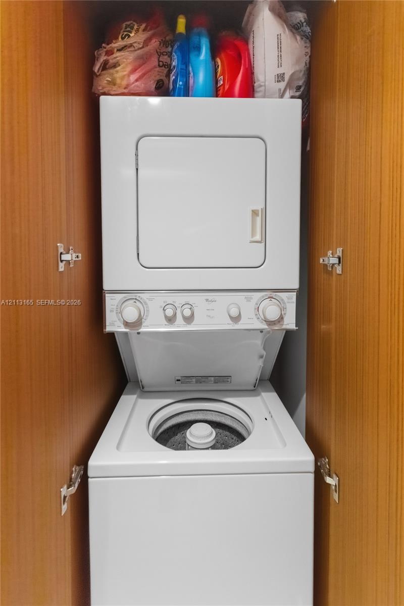 Stacked laundry unit enclosed within built-in cabinetry featuring wood-finish paneling and interior metal hinges
