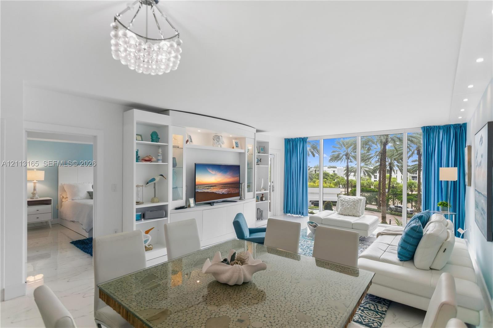 Open-concept interior featuring floor-to-ceiling windows, polished stone-finish flooring, custom built-in cabinetry with integrated shelving, and a decorative multi-tiered pendant light fixture