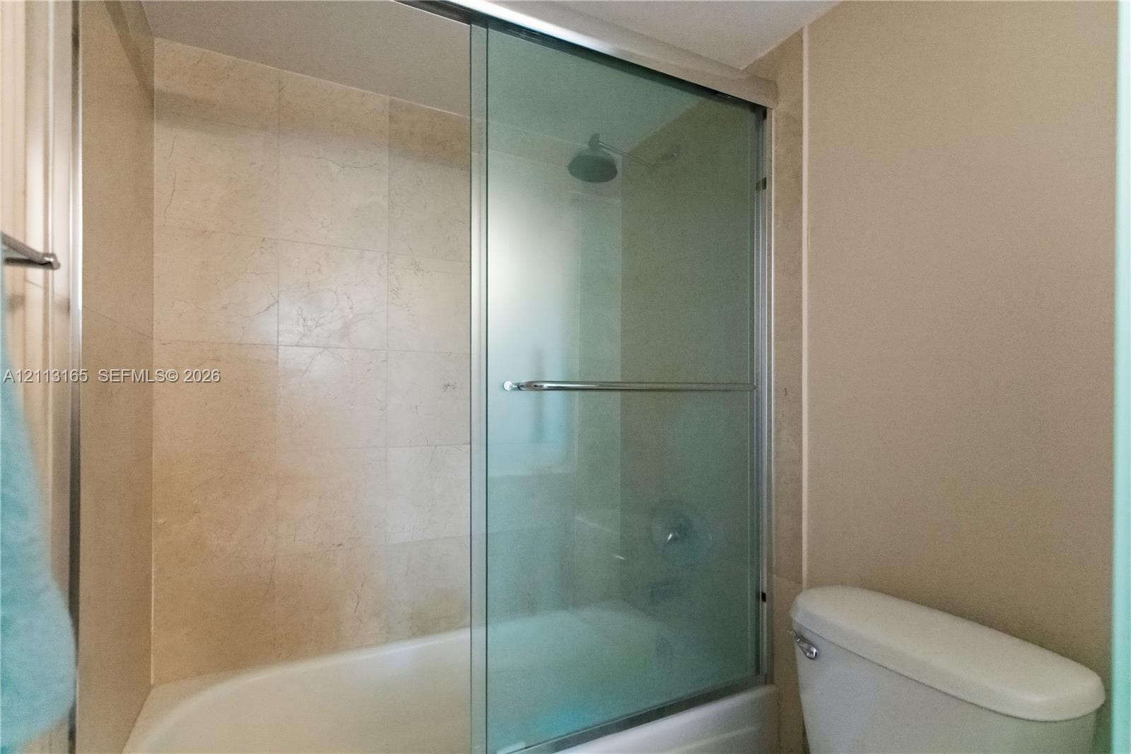 Shower-tub combination featuring floor-to-ceiling tile surround, sliding glass door, and a wall-mounted shower head