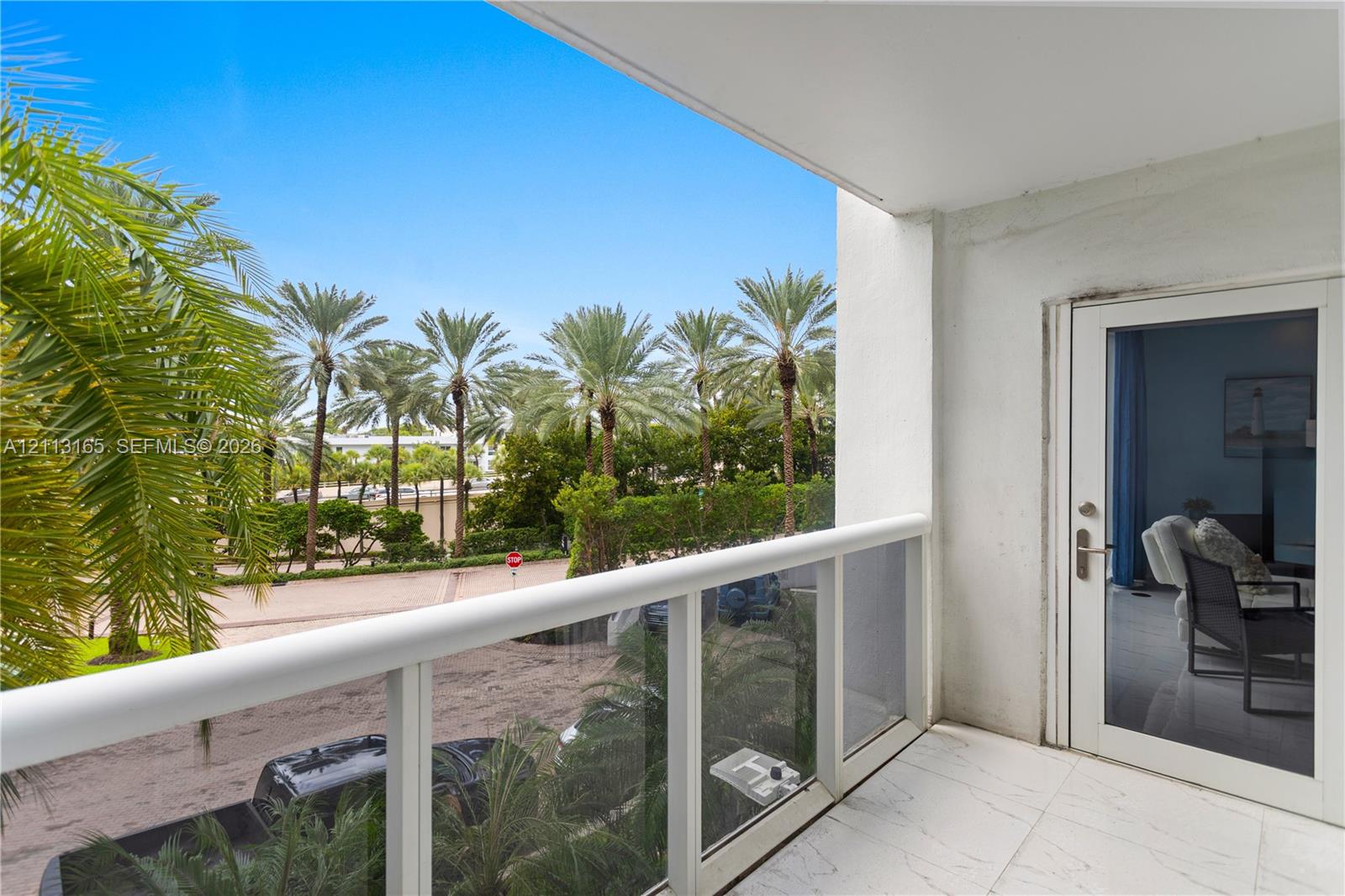 Covered balcony featuring white tiled flooring, a glass panel railing, and a full-height glass door entry