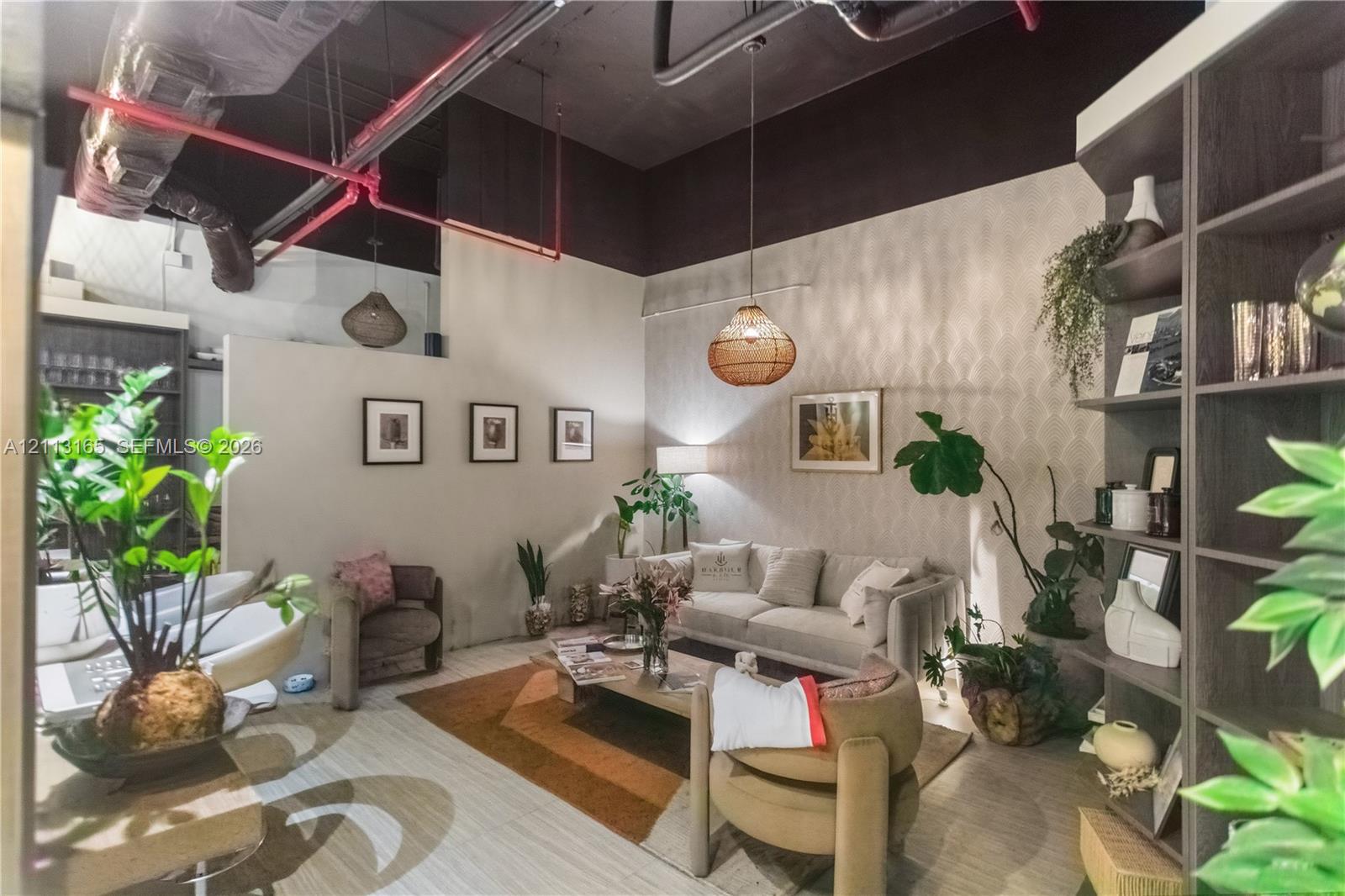 Industrial-style exposed ceiling with red fire suppression piping, high ceilings, custom built-in dark wood shelving unit, and patterned wallpaper accent wall