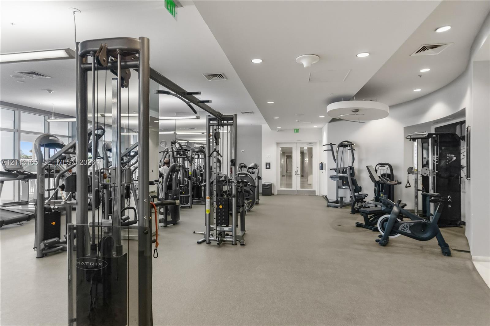 Fitness facility featuring rubberized flooring, recessed ceiling lighting, full-length mirrors, and glass double doors