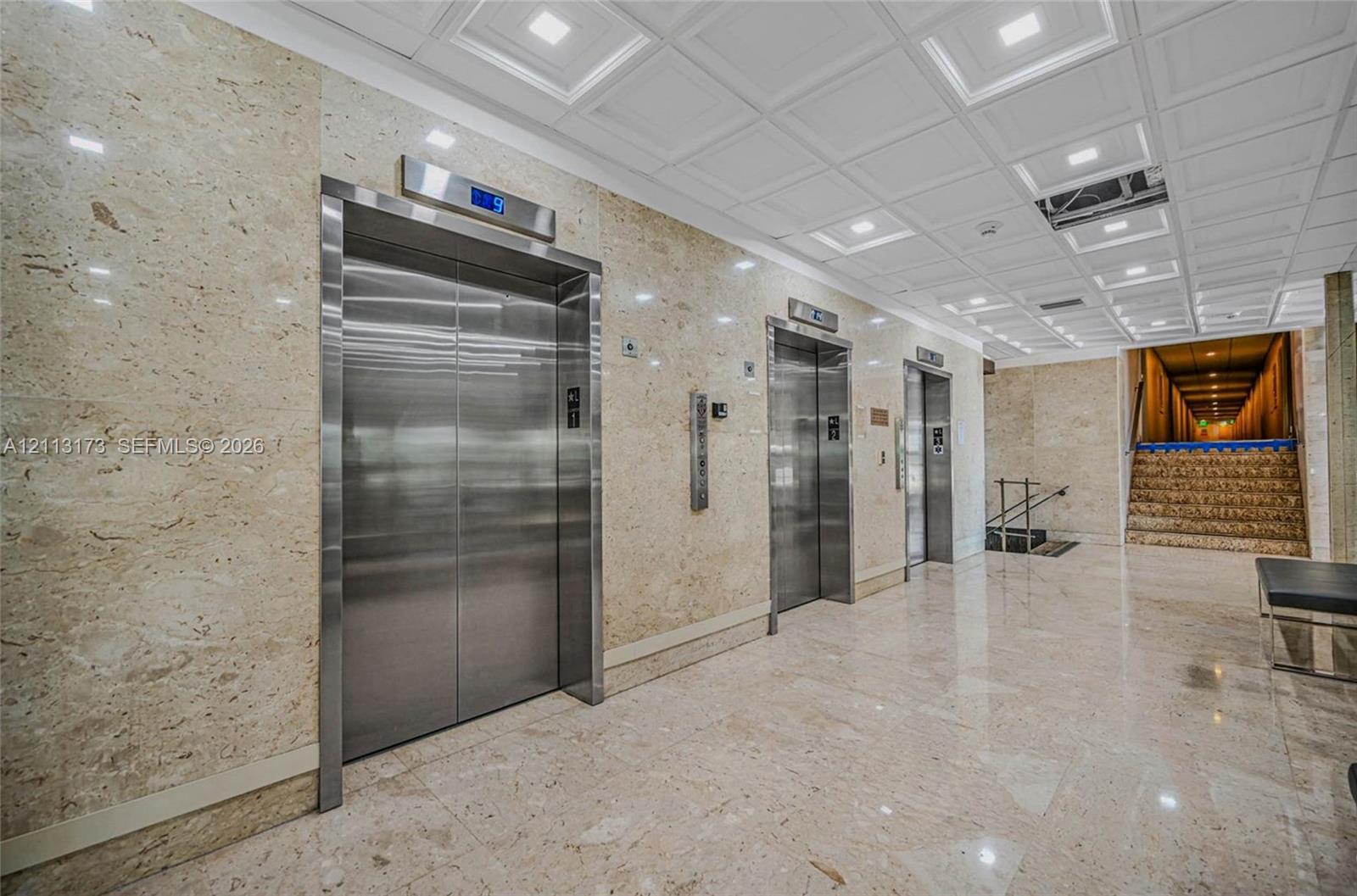 Polished stone wall cladding, stainless steel elevator doors, recessed ceiling lighting, coffered ceiling detail, and polished stone tile flooring Polished stone wall cladding, stainless steel elevator doors, recessed ceiling lighting, coffered ceiling detail, and polished stone tile flooring