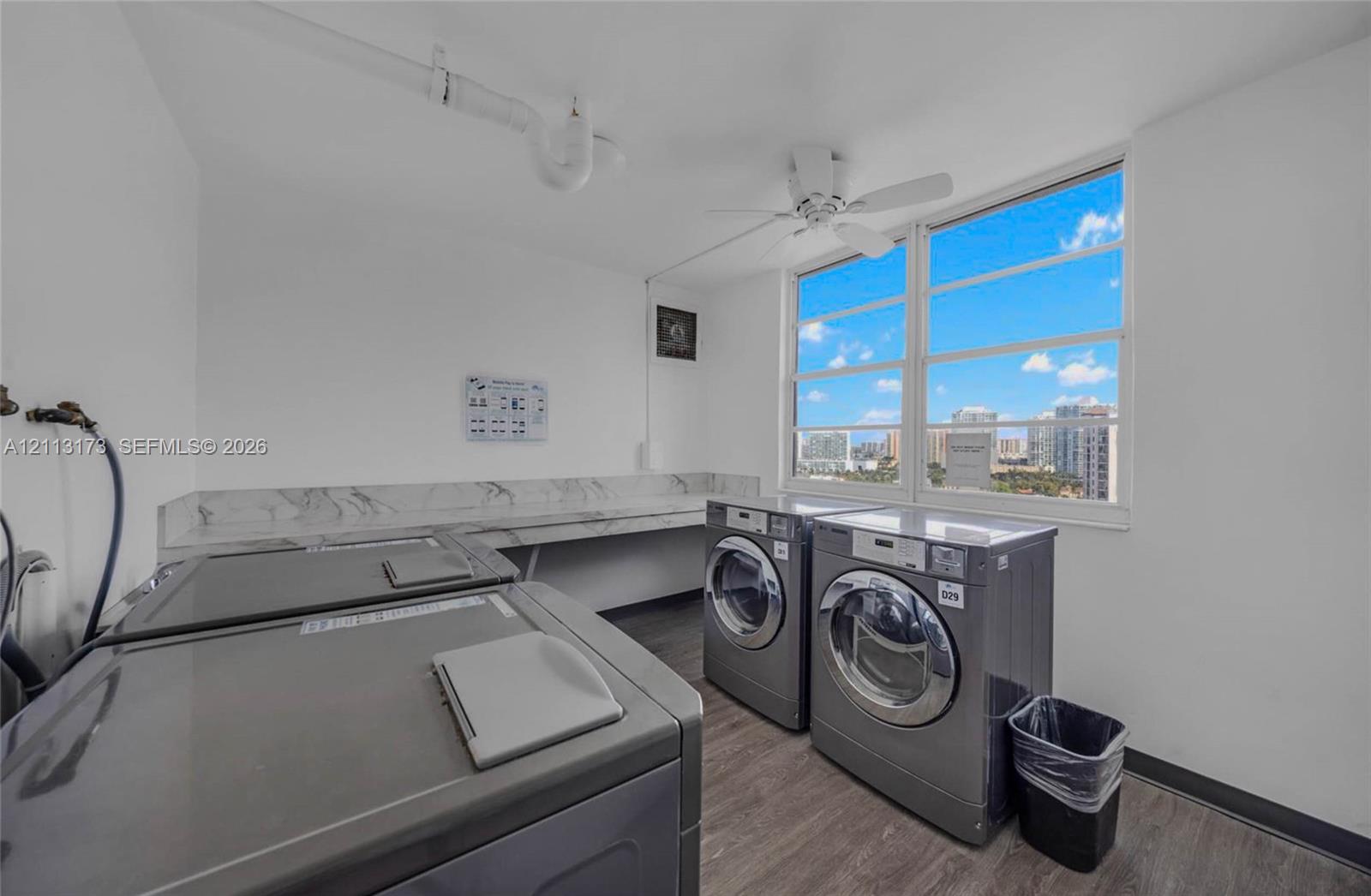 Laundry area featuring wood-finish flooring, a stone-patterned backsplash, large windows, and an attached ceiling fan