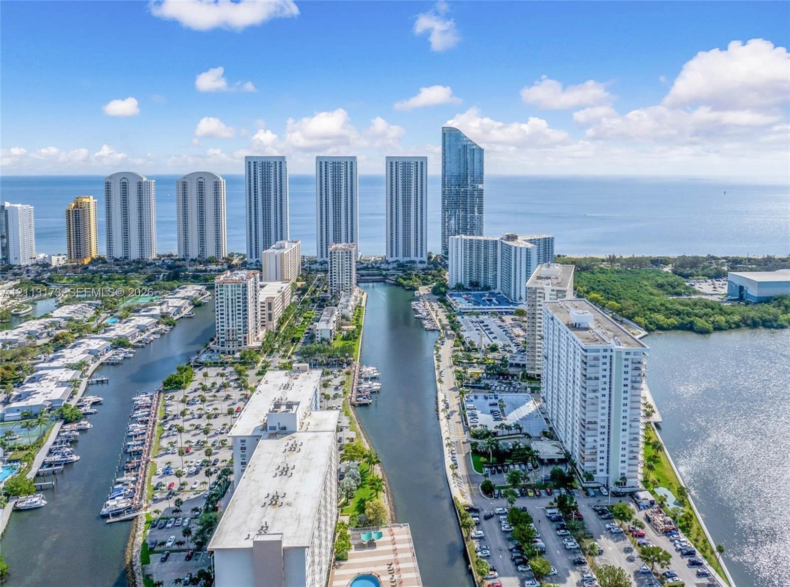 Aerial perspective of high-rise structures situated along an inlet, featuring direct water frontage, private boat docking, paved parking areas, and coastal surroundings Aerial perspective of high-rise structures situated along an inlet, featuring direct water frontage, private boat docking, paved parking areas, and coastal surroundings