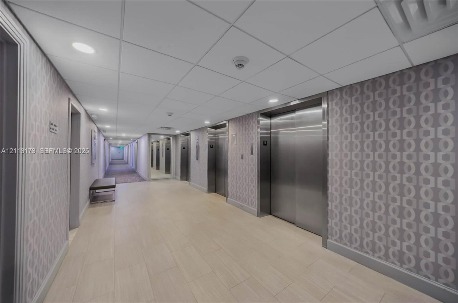 Hallway featuring tile flooring, patterned wall coverings, recessed lighting, and stainless steel elevator doors Hallway featuring tile flooring, patterned wall coverings, recessed lighting, and stainless steel elevator doors