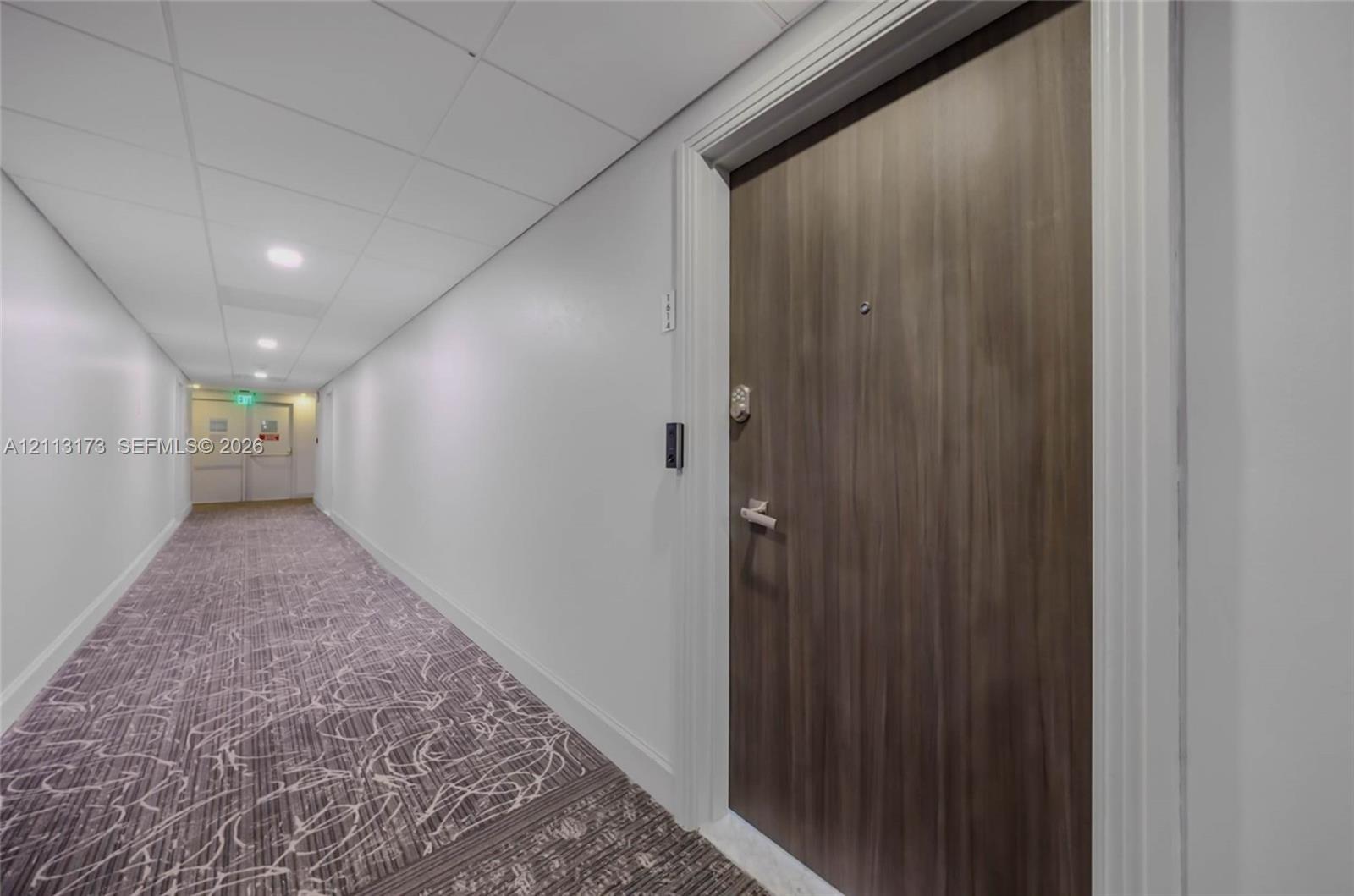 Wood-finish entry door with metal hardware, recessed ceiling lighting, and patterned carpeting Wood-finish entry door with metal hardware, recessed ceiling lighting, and patterned carpeting