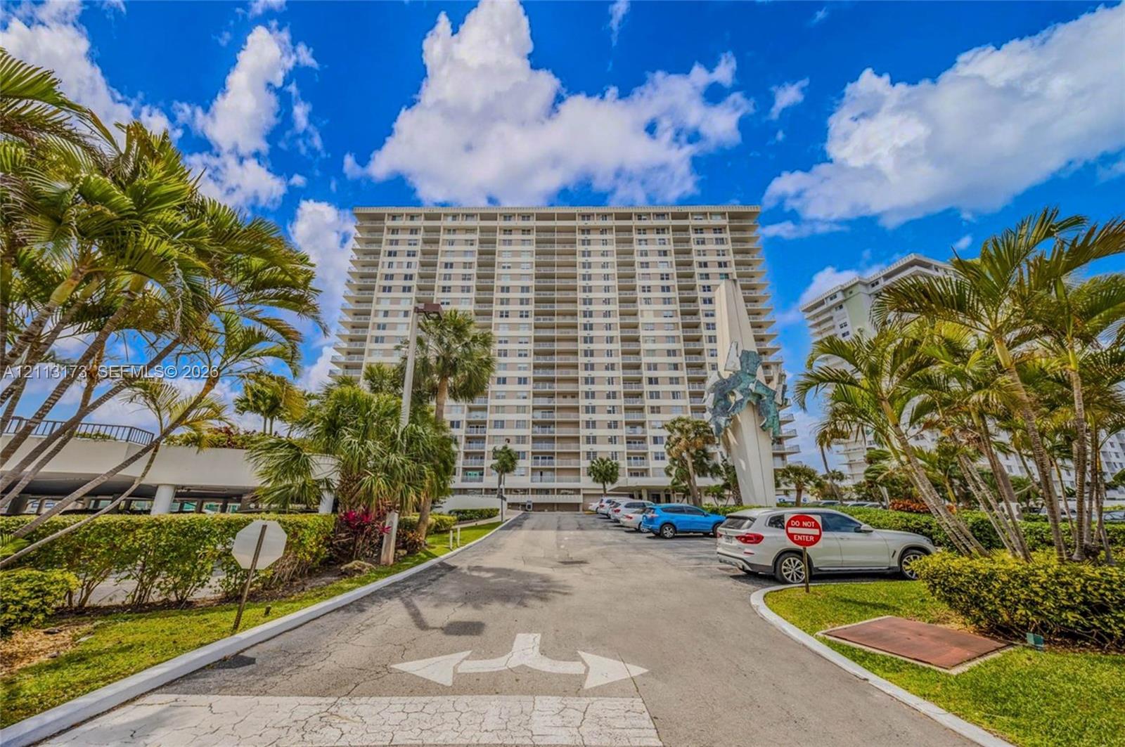 High-rise residential exterior featuring a multi-story facade, paved surface parking, integrated landscaping, and sculptural monument High-rise residential exterior featuring a multi-story facade, paved surface parking, integrated landscaping, and sculptural monument