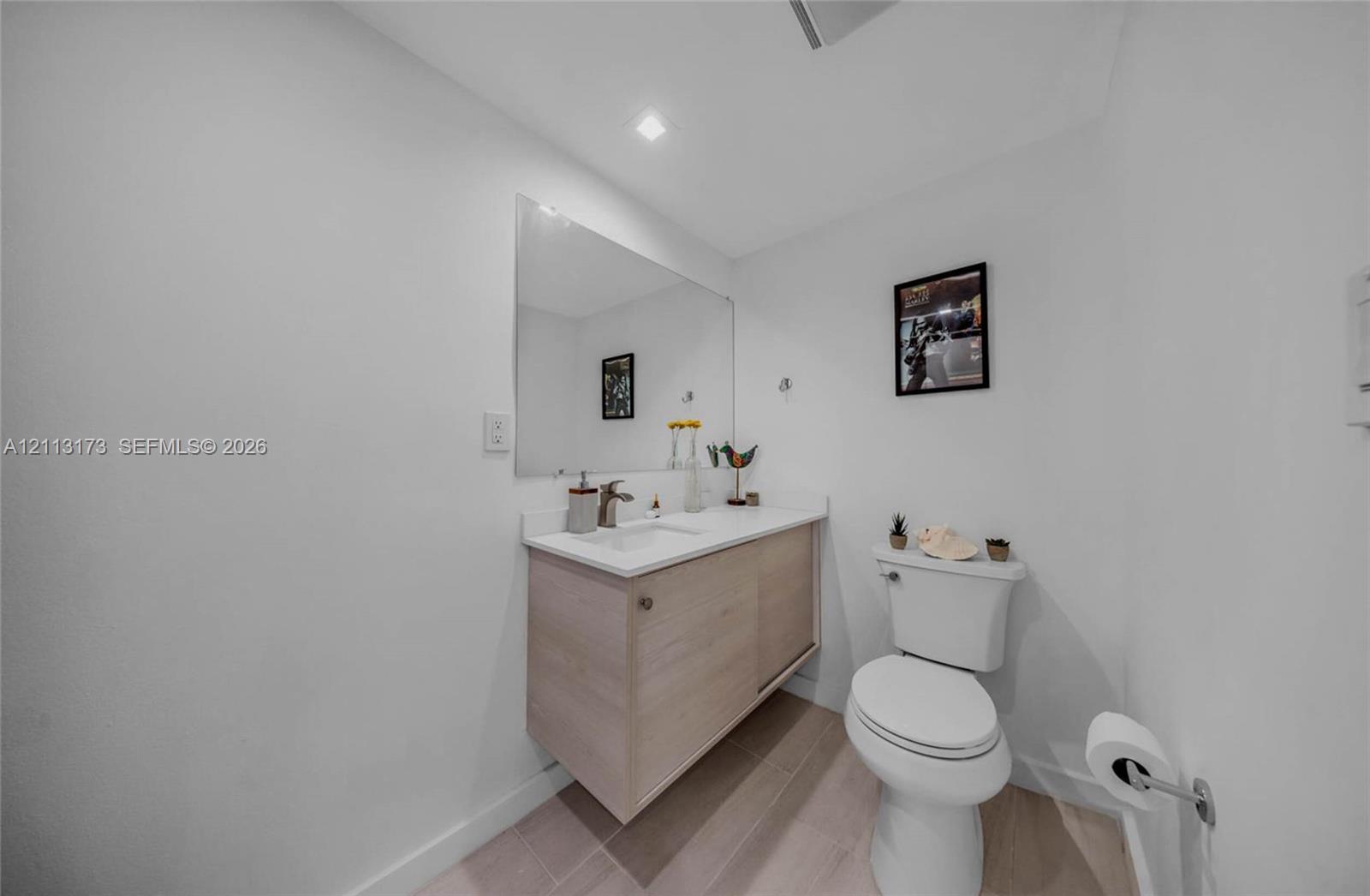 Floating vanity with a light wood finish, integrated white countertop with basin, wall-mounted mirror, recessed ceiling lighting, and neutral-toned flooring