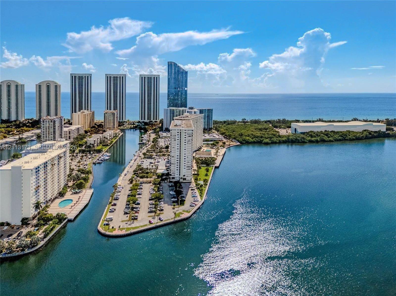 Aerial perspective of coastal high-rise development featuring waterfront positioning, expansive water frontage, and surrounding urban skyline